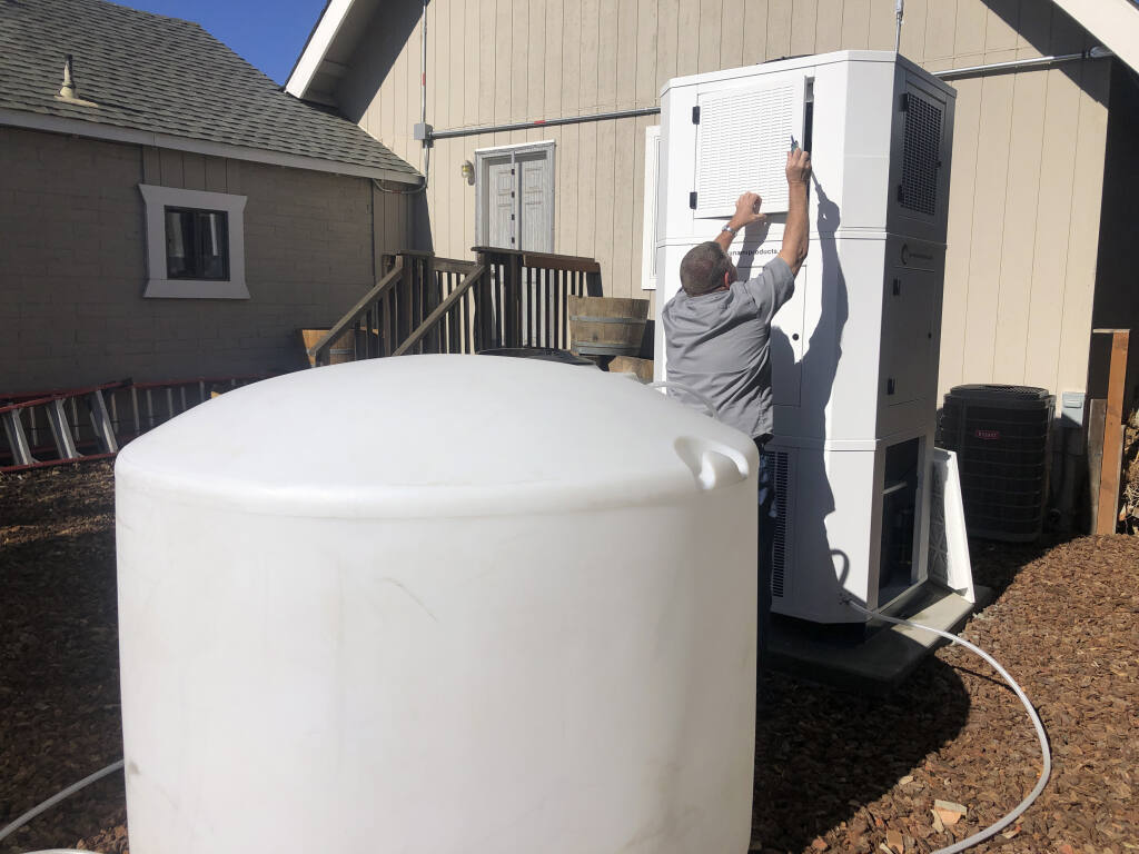 Ted Bowman, design engineer with Tsunami Products, installs a unit in homeowner Don Johnson's backyard in Benicia, Calif., Sept. 28, 2021. The recent invention can make water out of the air and in parched California, some homeowners are already buying the pricey devices. The air-to-water systems work like air conditioners by using coils to chill air, then collect water drops in a basin. (AP Photo/Haven Daily)