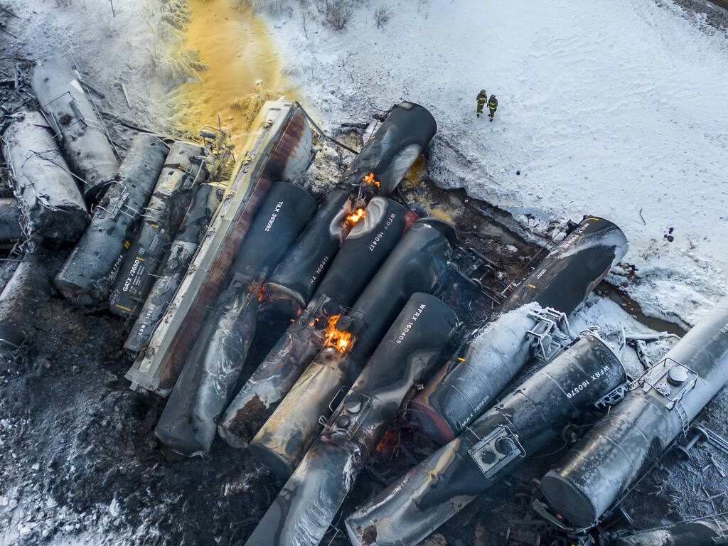Firefighters stand near piled up train cars, near Raymond, Minn., Thursday, March 30, 2023, the morning after a BNSF freight train derailed. Authorities say a train hauling ethanol and corn syrup derailed and caught fire and residents within 1/2 mile of the crash were ordered to evacuate from their homes. (Kerem Yücel/Minnesota Public Radio via AP)