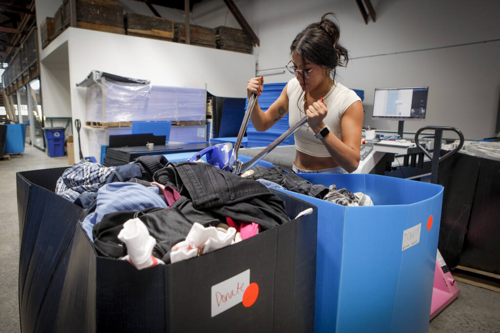 Lina Ortiz sorts through boxes of donated clothes in the NooNoo warehouse. NooNoo’s co-owners Semmelhack and Whalen want to ensure they aren’t adding to the problem of tons of wasted thrown-out clothing and work to responsibly pass on or discard anything they can’t use._ Monday, July 24, 2023._(CRISSY PASCUAL/ARGUS-COURIER STAFF)