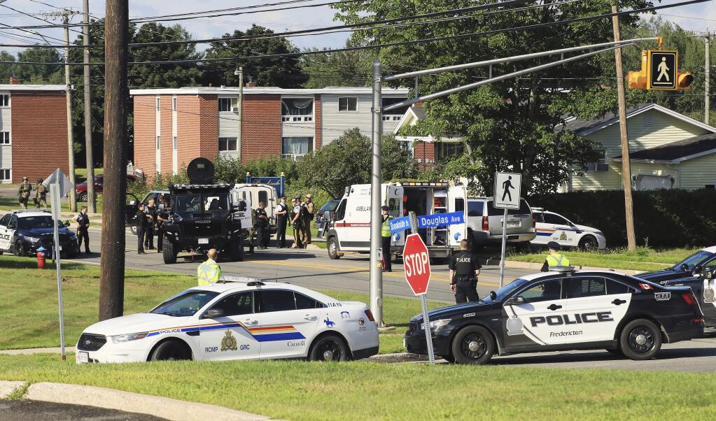 Police and RCMP officers survey the area of a shooting in Fredericton, New Brunswick, Canada on Friday, Aug. 10, 2018. Fredericton police say two officers were among four people who died in a shooting Friday in a residential area on the city's north side. One person was in custody, they said, and there was no further threat to the public. (Keith Minchin/The Canadian Press via AP)