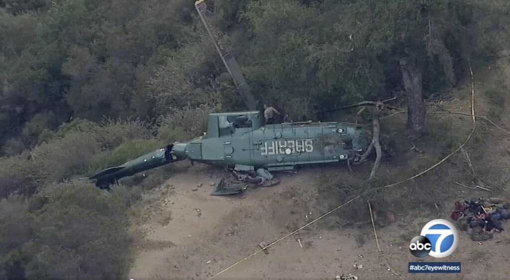 This ABC7 Los Angeles aerial video image shows emergency personnel next to a Los Angeles Sheriff Department helicopter after it crashed near San Gabriel dam in Azusa, Calif., on Saturday, March 19, 2022. Authorities are investigating the crash of a Los Angeles County Sheriff's Department rescue helicopter that left six people injured in mountains northeast of downtown LA. The department's Air Rescue 5 helicopter crashed shortly before 5 p.m. Saturday while responding to a vehicle that rolled over on a winding road in Angeles National Forest. (ABC7 Los Angeles via AP)