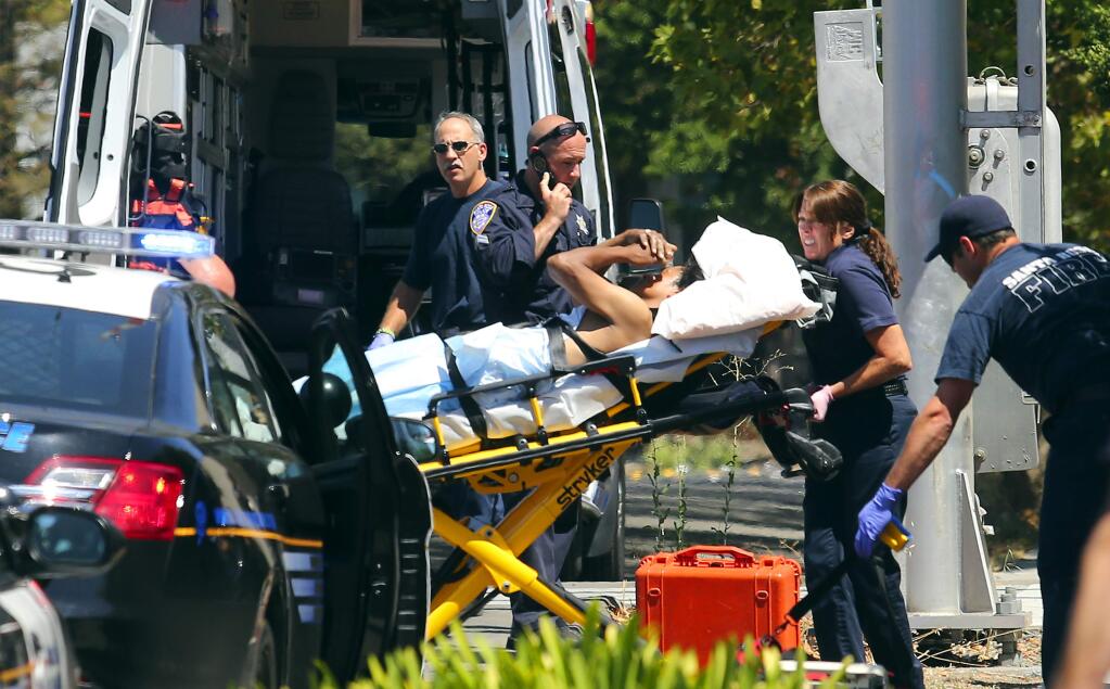 Medical personnel load a victim of a machete stabbing into an ambulance at the railroad tracks on Piner Rd. in Santa Rosa on Saturday afternoon. (JOHN BURGESS / The Press Democrat)