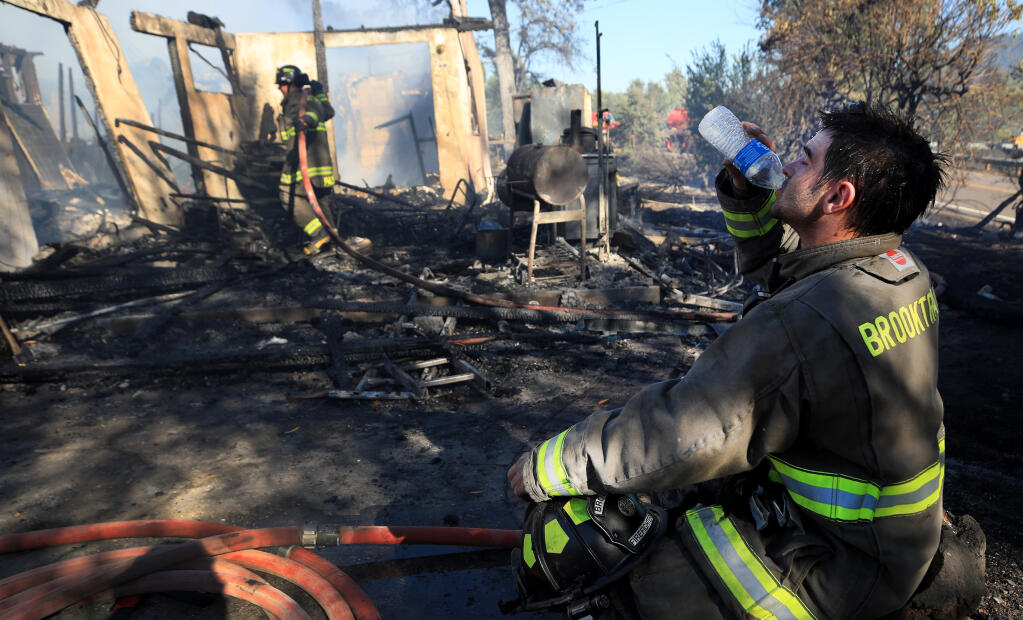 David Wells of the Brooktrails Township Fire Department in Willits hydrates after working to douse flames at home on Uva Drive and West School Way in Redwood Valley that was ignited by a wind-whipped brush fire on Wednesday, July 7, 2021. (Kent Porter / The Press Democrat)
