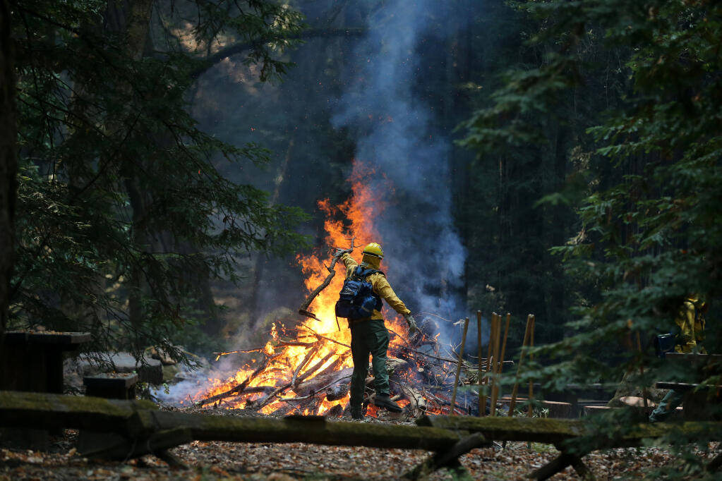 A National Guard member throws a branch on a bonfire as crews work to break down and burn fallen trees and debris at  Armstrong Woods State Natural Reserve in Guerneville, Calif., on Monday, August 31, 2020. (BETH SCHLANKER/ The Press Democrat)