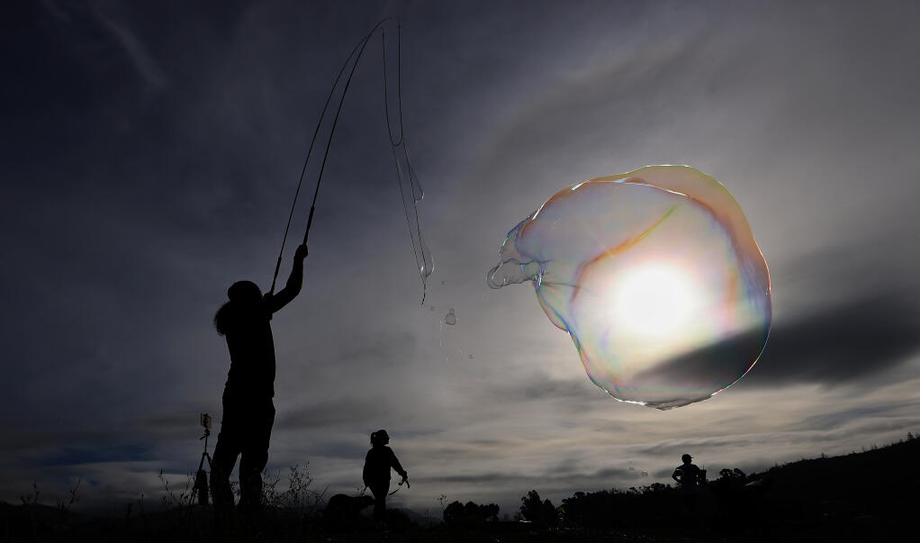 Travis Murphy of Santa Rosa uses the trail on Spring Lake dam as his bubble palette, Saturday, Oct. 14, 2023, as clouds part and the annular eclipse begins to darken the sky. Travis had no idea the annular eclipse was Saturday.  (Kent Porter / The Press Democrat)