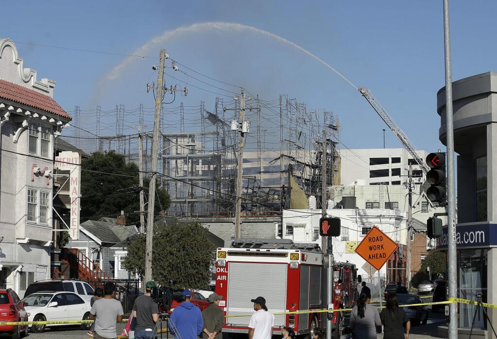 Firefighters spray a building in Oakland, Calif., Friday, July 7, 2017. A huge fire at the building under construction in Oakland has been contained early Friday, but evacuations remain in place at nearby buildings. (AP Photo/Jeff Chiu)