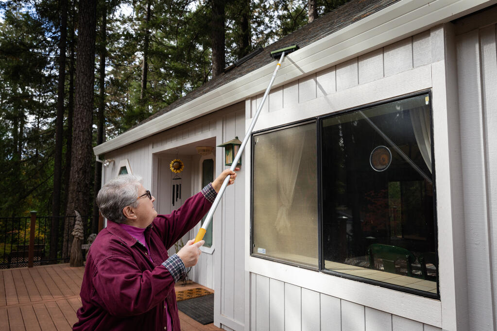 Donna Yutzy cleans the gutters of her home from flammable debris in the Magalia area of Butte County on Nov. 4, 2023. State law prohibits the use of landscaping plants and any flammable materials within a five-foot radius of the house. Photo by Manuel Orbegozo for CalMatters