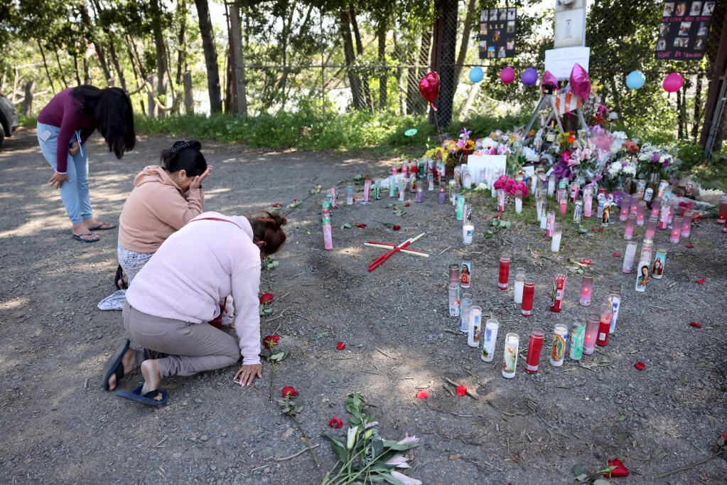 (From front) Noelia Serrano, Ilda Choc and her niece Angelica Choc pray near the site on Riverside Drive where a 17-year-old girl and 19-year-old woman were found fatally shot Sunday. Photo taken in Napa, Tuesday, April 16, 2024. (Beth Schlanker / The Press Democrat)