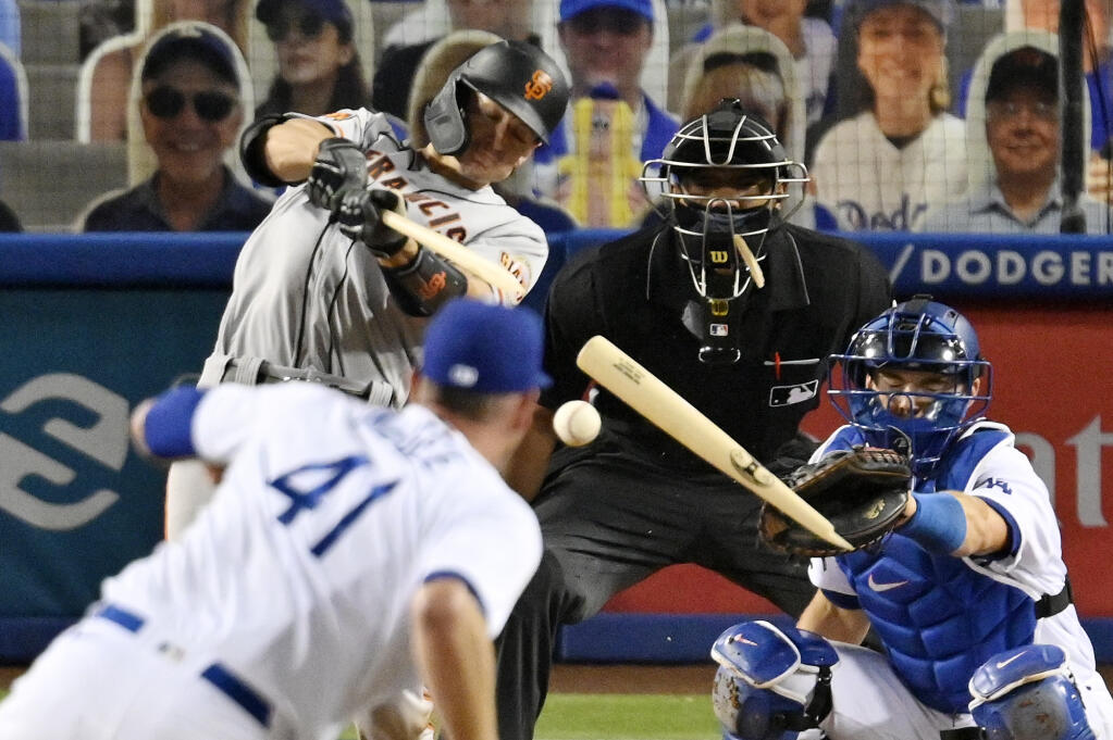 San Francisco Giants' Rob Brantly, left, breaks his bat as Los Angeles Dodgers relief pitcher Edubray Ramos, second from left, watches along with catcher Will Smith, right, and home plate umpire Edwin Moscoso during the eighth inning of a baseball game Friday, July 24, 2020, in Los Angeles. Brantly was thrown out at first on the play. (AP Photo/Mark J. Terrill)