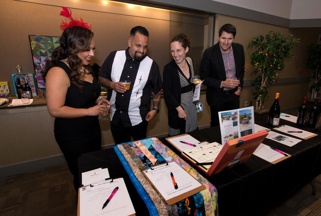 Indira and Juan Medina, left, laugh with Alyssa Kenney-Roe and Francisco Azevedo, right, all of Santa Rosa, as they look at silent auction items during the Gala Americana benefit for the Cesar Chavez Language Academy held at Friedman Event Center, Saturday, April 29, 2023, in Santa Rosa. (Darryl Bush / For The Press Democrat)