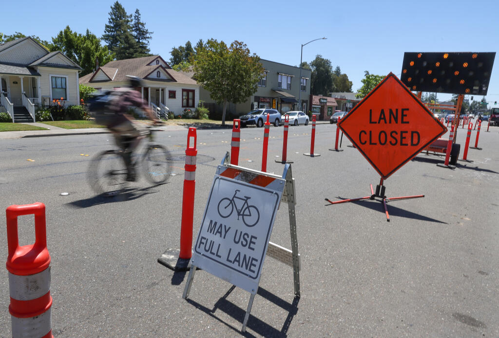 A cyclist rides along the one lane of southbound traffic on Santa Rosa Avenue, near Wheeler Street, as a road improvement project gets underway in Santa Rosa, Friday, July 14, 2023. (Christopher Chung / The Press Democrat)