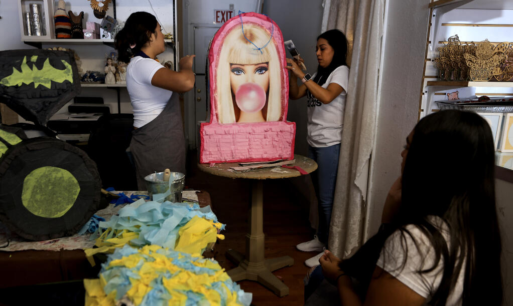 Angelene García, de 17 años, izquierda, ayuda a su madre Anahí Silva, derecha, a completar una piñata de Barbie, mientras Brisbany García, de 13 años, se toma un descanso de trabajar en otra pieza personalizada en Clearlake, el miércoles 2 de agosto de 2023. (Kent Porter / The Press Democrat) 2023