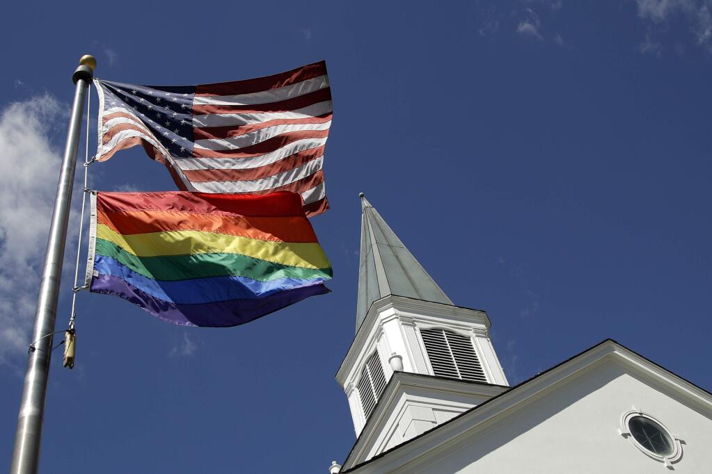 FILE - In this April 19, 2019, file photo, a gay pride rainbow flag flies along with the U.S. flag in front of the Asbury United Methodist Church in Prairie Village, Kan., United Methodist Church leaders are proposing creation of a separate division that would let more traditional denominations break away because of the disagreement with churches over the UMC's official stance on gay marriage. (AP Photo/Charlie Riedel, File)