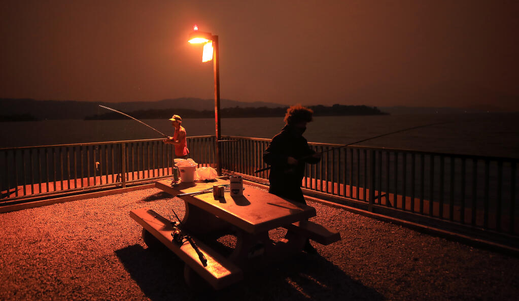 Eric Austin of Clearlake Oaks, left, and Chance Martin of Antioch prepare to cast their lines in to Clear Lake under an eerie smoky orange sunset, Monday, August 31, 2020 in Clearlake Oaks. The smoke from area wildfires has the Air Quality Index way past unhealthy levels, earlier in the day Mt. Konocti, barely visible on the right, recorded an AQI of 400.  (Kent Porter / The Press Democrat) 2020