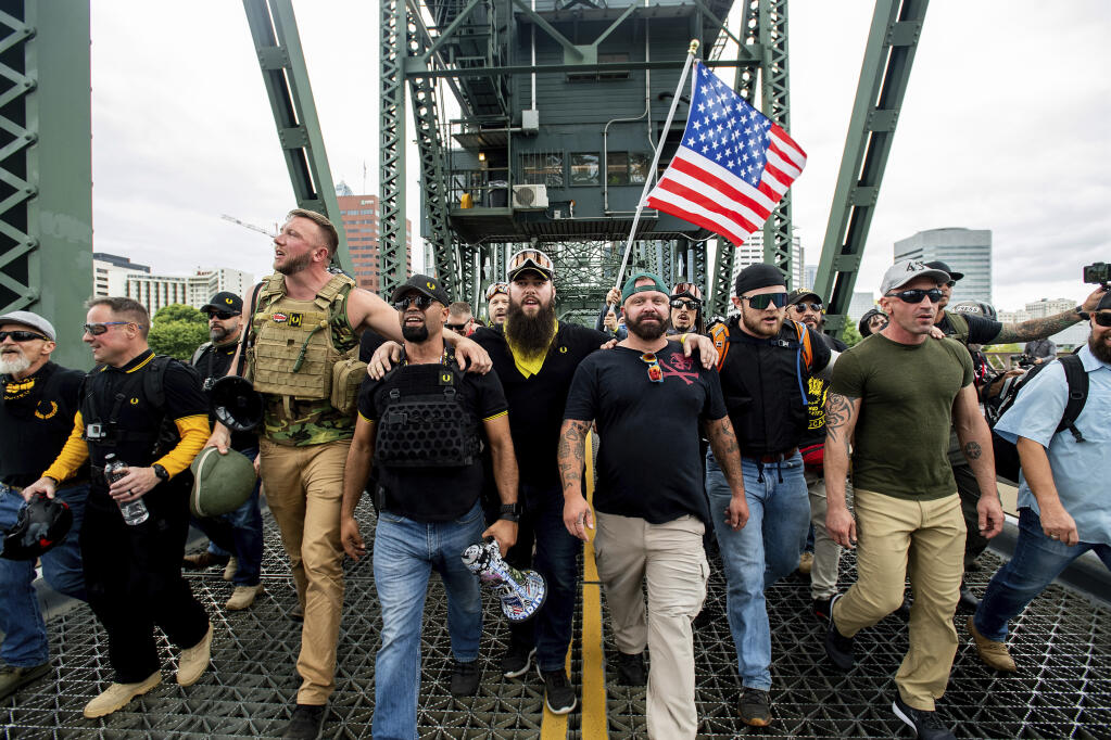 FILE - In this Aug. 17, 2019, file photo, members of the Proud Boys and other right-wing demonstrators march across the Hawthorne Bridge during a rally in Portland, Ore. The group includes organizer Joe Biggs, in green hat, and Proud Boys Chairman Enrique Tarrio, holding megaphone. At least several thousand people are expected in Portland on Saturday, Sept. 26, 2020, for a rally in support of President Donald Trump and his re-election campaign as tensions boil over nationwide following the decision not to charge officers in Louisville, Kentucky for killing Breonna Taylor. (AP Photo/Noah Berger, File)