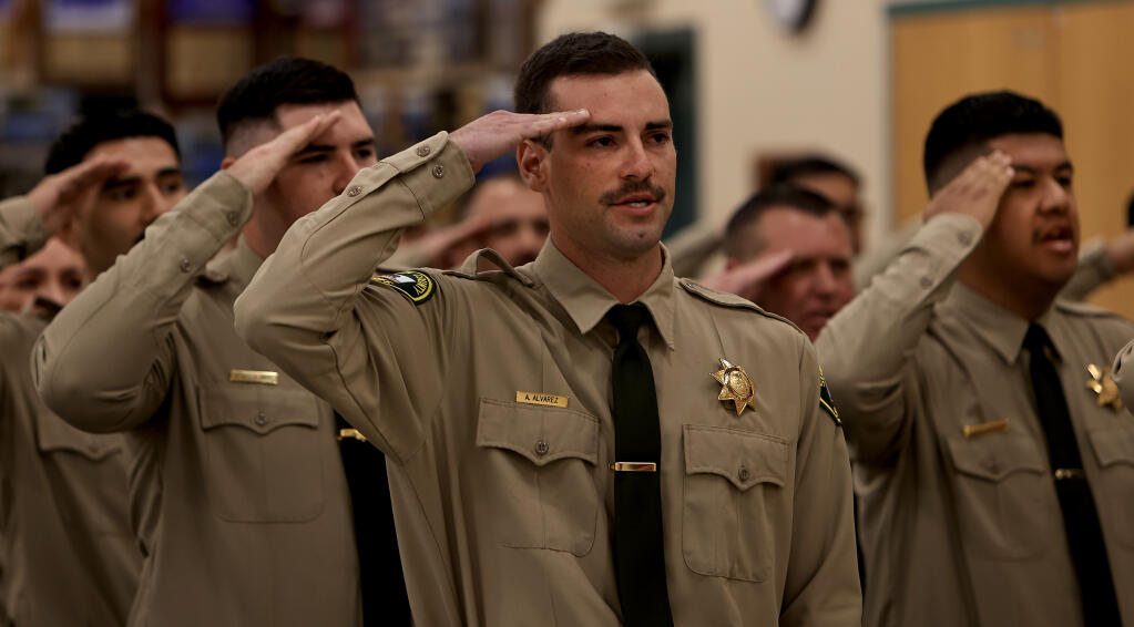 Austin Alvarez, front, with his fellow graduates, salute during the Pledge of Allegiance during their graduation as corrections officer deputies from the Santa Rosa Junior College Public Safety Training Center in Windsor, Friday, April 26, 2024. (Kent Porter / The Press Democrat)