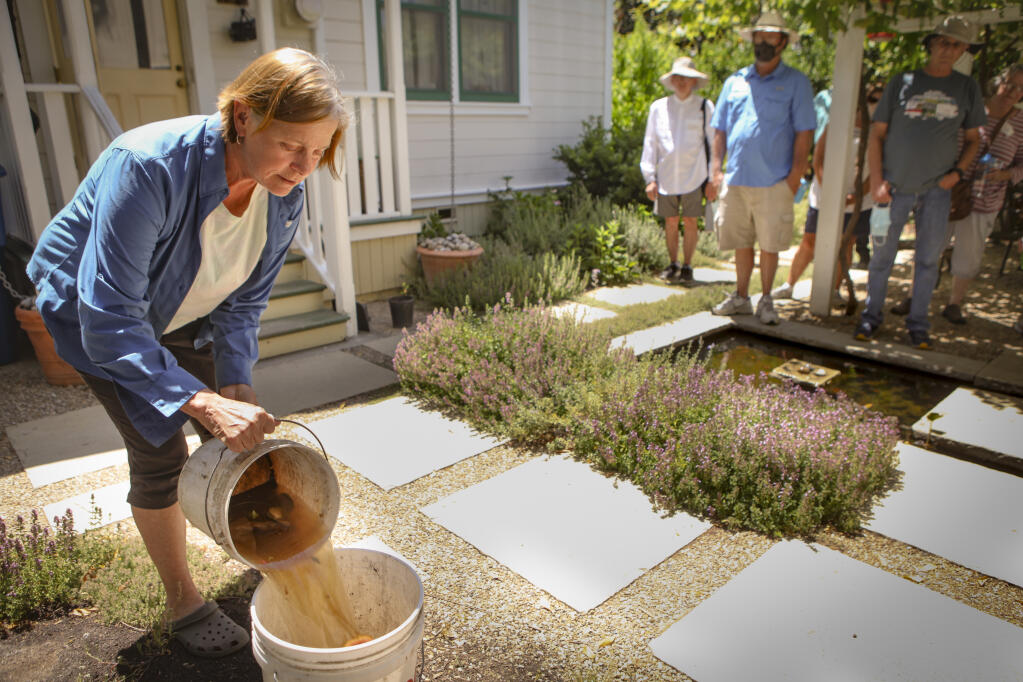 Eberle Ewing talks to the group of Daily Acts’ guests who toured Petaluma homes that use graywater to water their landscape. Ewing showed them another water conservation technique she also uses for her trees using kitchen sink water collected in a bucket. (CRISSY PASCUAL/ARGUS-COURIER STAFF)