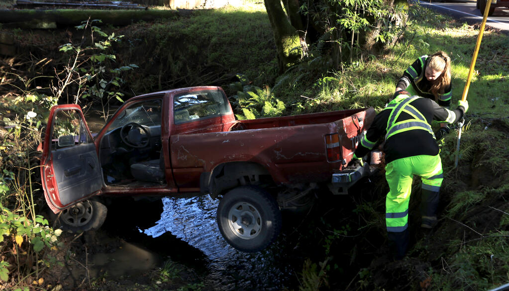 Sebastopol Tow personnel hook cables to drag a truck out of a tributary to Atascadero Creek along Bodega Highway at Furlong Road west of Sebastopol, Friday, Dec. 22, 2023. One person was extricated from the vehicle by Gold Ridge Fire Protection District and transported to an area hospital. (Kent Porter / The Press Democrat) 2023