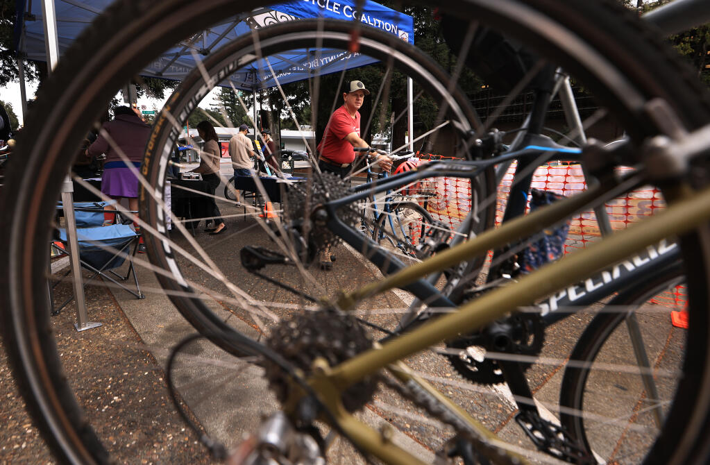 Jon Dick with the Sonoma County Bicycle Coalition moves a bike in to a valet service spot, as they take over three parking spaces on Fourth Street in Santa Rosa, Saturday, Oct, 21, 2023, in front of Sonoma Clean Power’s Advanced Energy Center.  (Kent Porter / The Press Democrat)