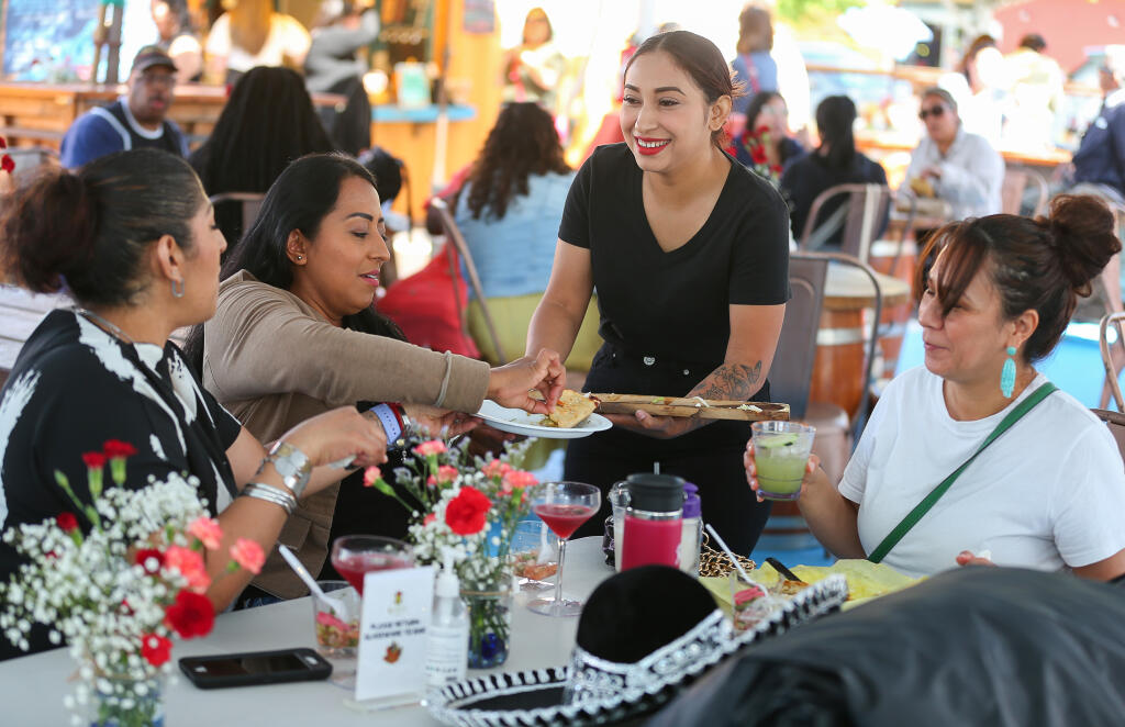 Gladys Romero, standing, offers quesadillas to Esmeralda Garcia, left, Nancy Arango, and Eva Avila during a party to celebrate the one-year anniversary of Mitote Food Park in the Roseland area of Santa Rosa on Thursday, June 15, 2023.  (Christopher Chung/The Press Democrat)