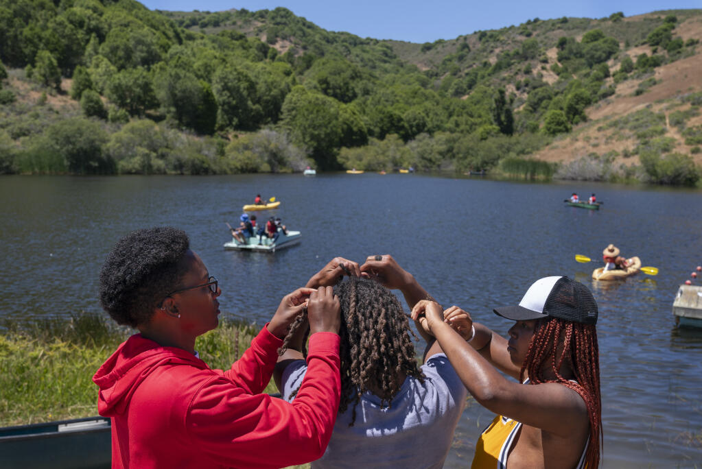Camp sports director Cellie Davis, 39, left, of Houston, and counselor Satya Sheftel-Gomes, 22, of San Francisco, right, undo the two-strand-twists from the locs in the hair of 17-year-old junior counselor Jordan Gardner, of Novato, Calif., as campers enjoy the lake at Camp Be’chol Lashon, a sleepaway camp for Jewish children of color, Friday, July 28, 2023, at Walker Creek Ranch in west Marin County. (AP Photo/Jacquelyn Martin)