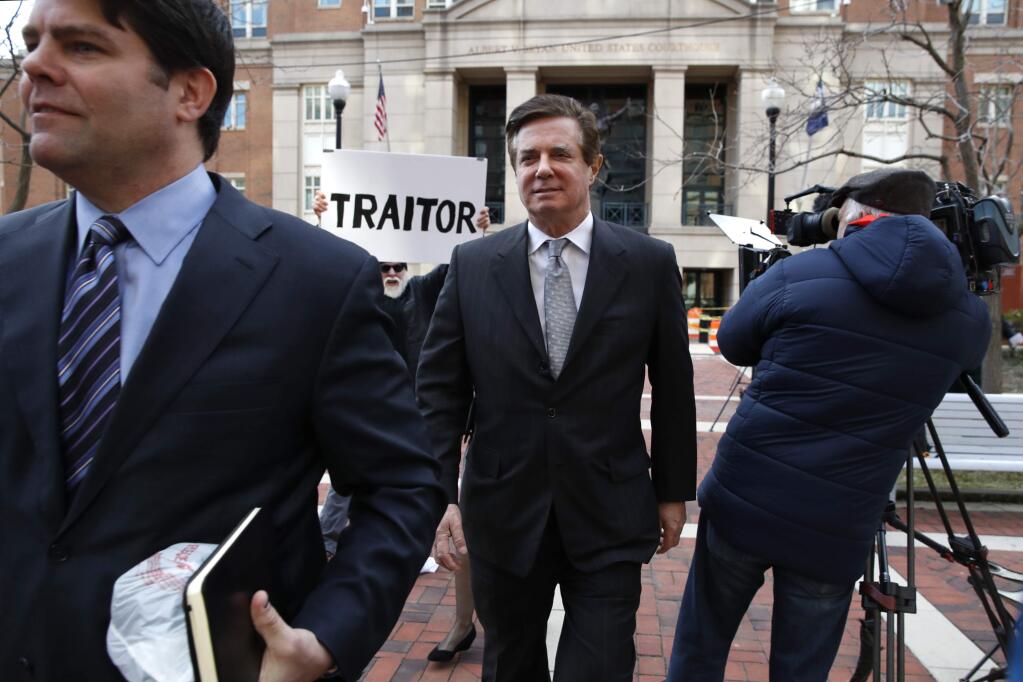 FILE - In this March 8, 2018, file photo, Jason Maloni, left, former Trump campaign chairman Paul Manafort's spokesman, left, walks with Paul Manafort, center, as they leave the Alexandria Federal Courthouse after an arraignment hearing in Alexandria, Va. A federal judge in Virginia has rejected Manfort's move to throw out charges brought by the special counsel in the Russia investigation. The decision June 26 was a setback for Manafort in his defense against numerous tax and bank fraud charges. Behind Manafort protester Bill Christeson holds up a sign that says 'traitor.' (AP Photo/Jacquelyn Martin)