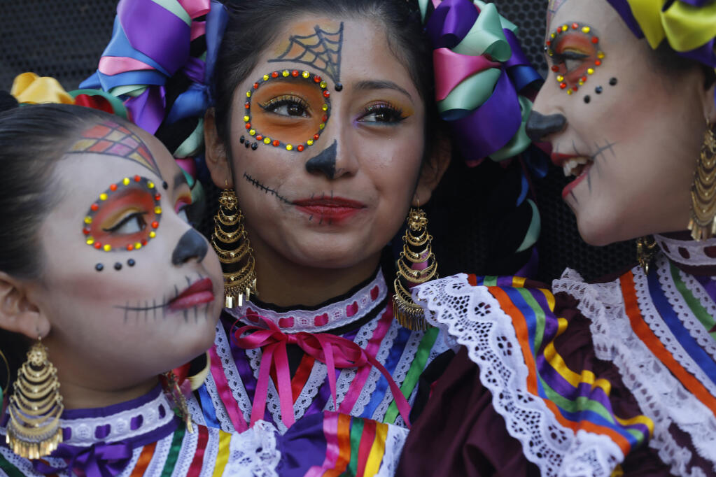(From left) Dancers Yuliana Gutierrez, 10, Natalia Soriano, 15, and Tania Escobar watch a performance from offstage during the Día de los Muertos at the Plaza in Healdsburg, Calif. on Sunday, October 30, 2022. (Beth Schlanker/The Press Democrat)