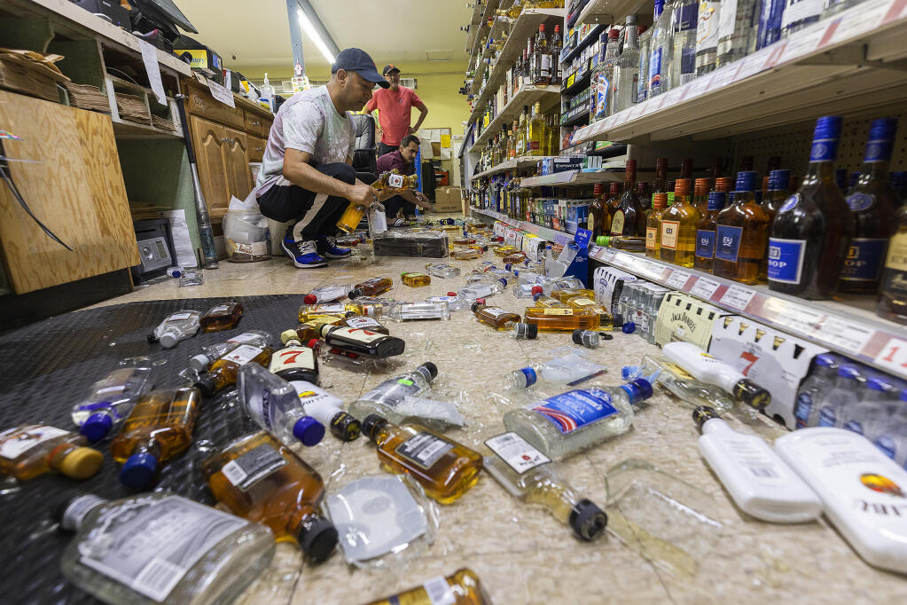 Paul Pankaj cleans up bottles of liquor that fell from the shelves at Sam’s Market on Humboldt Street in Santa Rosa  after an early evening earthquake Tuesday, September 13, 2022.  (John Burgess/The Press Democrat)