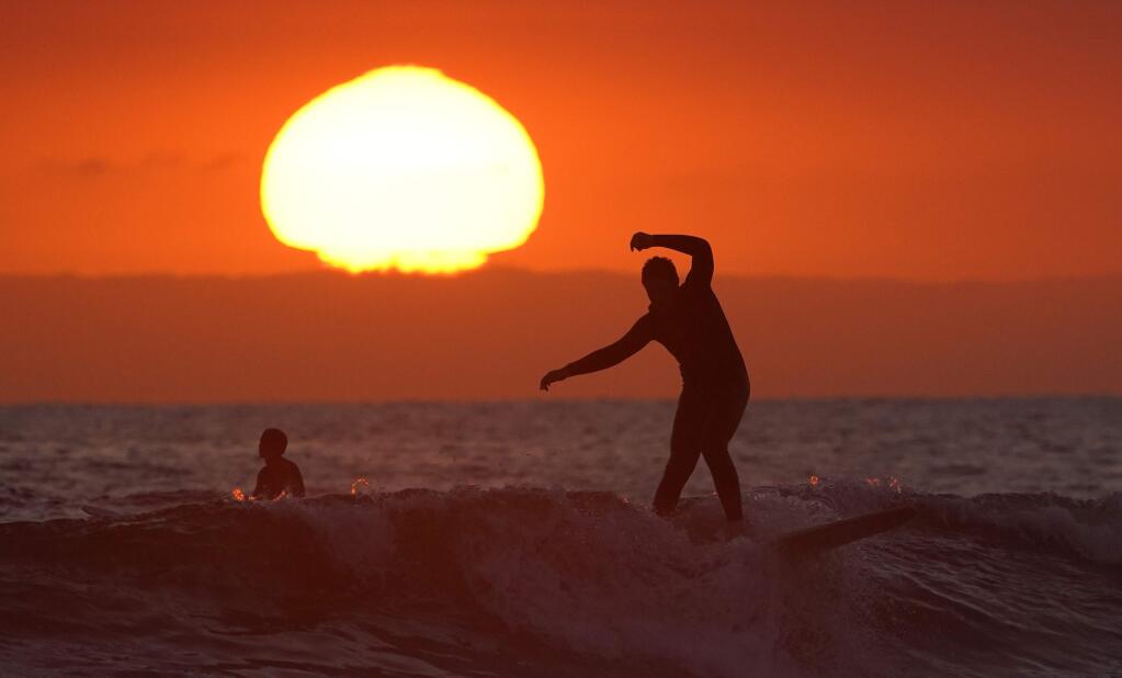 A surfer rides a wave as the sun goes down Thursday, April 30, 2020, in Newport Beach, Calif. The beach is one of the beaches kept open during the coronavirus outbreak. While some communities in Orange County have closed beaches, Huntington Beach and Newport Beach refused to limit access. (AP Photo/Mark J. Terrill)