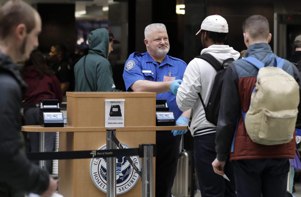 A TSA worker checks hands an identification card back to a traveler, Friday, Jan. 25, 2019, at Seattle-Tacoma International Airport in Seattle. Yielding to mounting pressure and growing disruption, President Donald Trump and congressional leaders on Friday reached a short-term deal to reopen the government for three weeks while negotiations continue over the president's demands for money to build his long-promised wall at the U.S.-Mexico border. (AP Photo/Ted S. Warren)