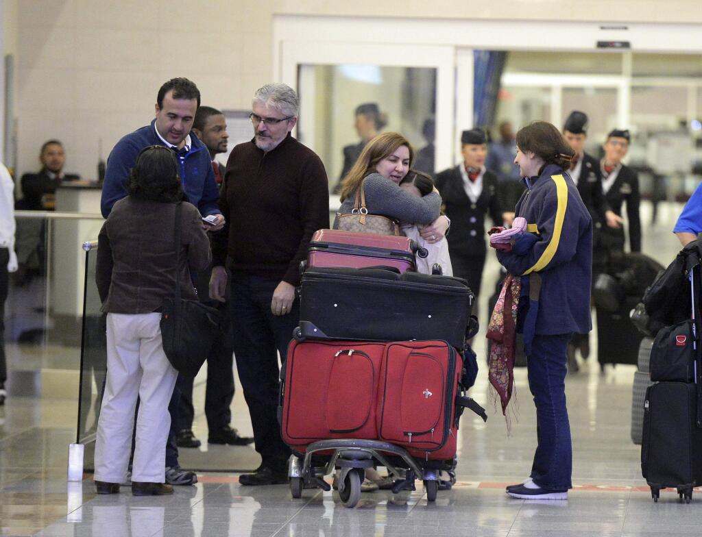 FILE - In this Saturday, Jan. 25, 2017, file photo, Mansour Kenereh, center, reunites with family members in the international arrivals lobby at Hartsfield- Jackson Atlanta International Airport, in Atlanta. The family of three were among several people detained at the U.S. Customs and Border Protection office following an executive order from President Donald Trump limiting immigration. Trump's executive order suspending immigration from seven majority-Muslim countries could slow the U.S. economy by hampering two of the nation's top export industries: Tourism and higher education. (Kent D. Johnson/Atlanta Journal-Constitution via AP, File)