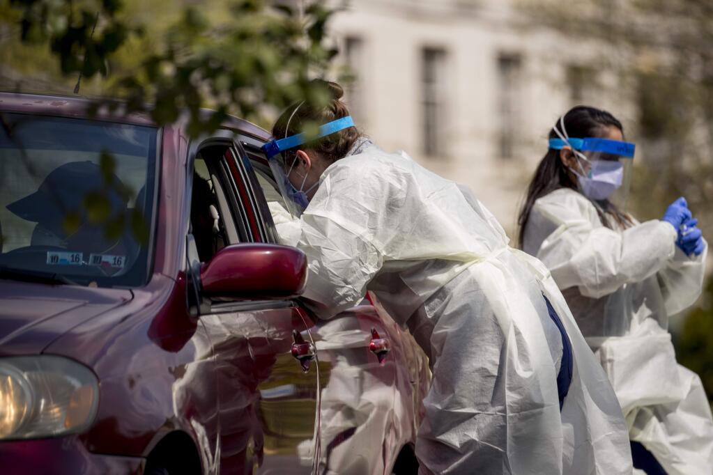 A medical worker tests a young man for COVID-19 at a Children's National Hospital drive-through (drive-in) coronavirus testing site at Trinity University, Thursday, April 16, 2020, in Washington. (AP Photo/Andrew Harnik)