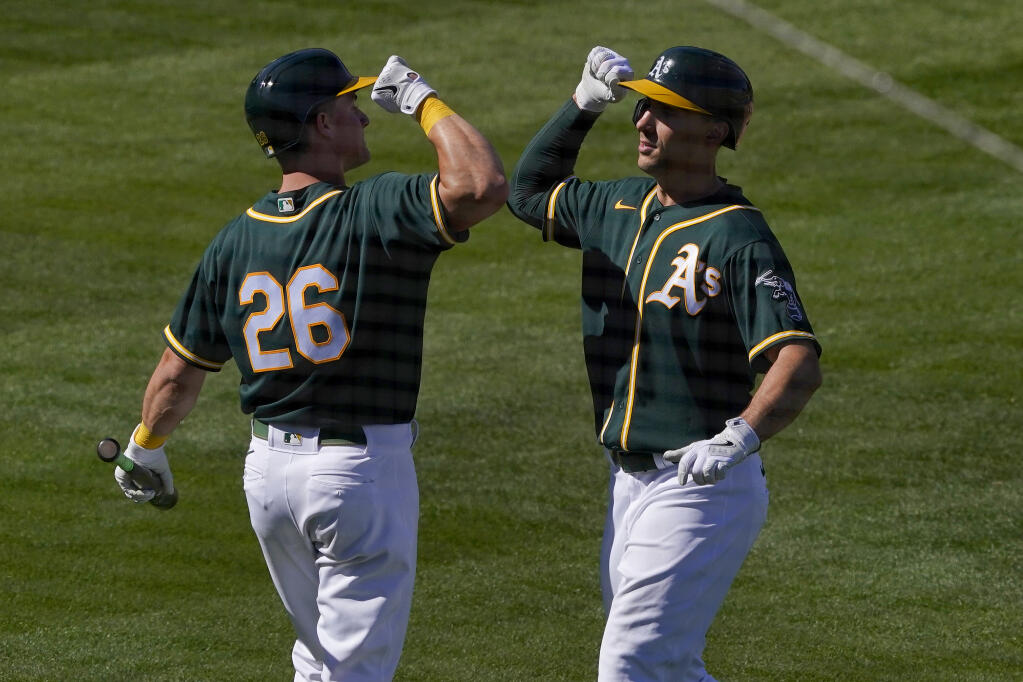The Oakland Athletics’ Matt Chapman, left, greets Matt Olson after hitting a solo home run against the Los Angeles Angels during the third inning of a spring training game on Friday, March 5, 2021, in Mesa, Arizona. (Matt York / ASSOCIATED PRESS)