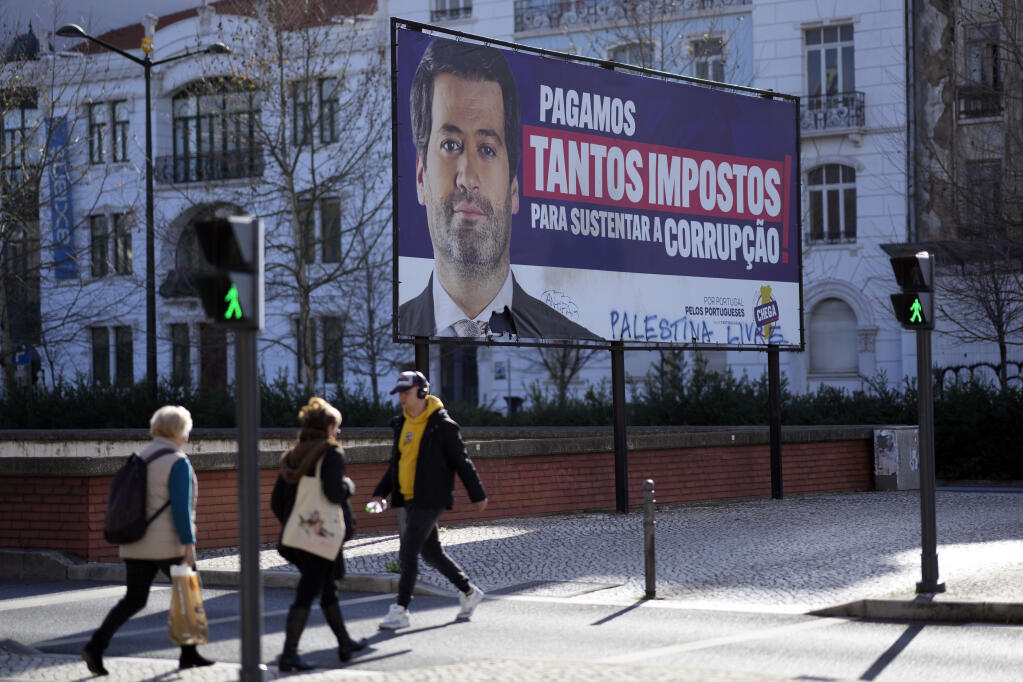 FILE - People walk by a billboard for Andre Ventura, leader of populist radical right party Chega (in English, Enough) with the words, "We pay so many taxes to sustain corruption", in Lisbon, March 4, 2024. (AP Photo/Armando Franca, File)