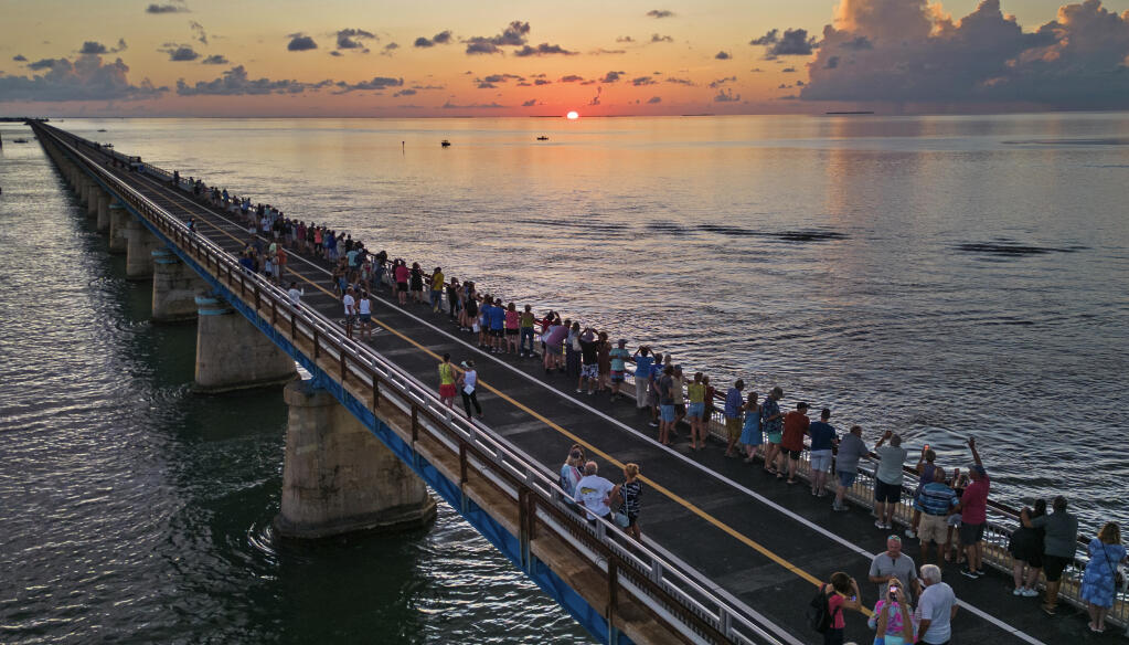 In this aerial photo provided by the Florida Keys News Bureau, attendees watch and toast the sunset at a Florida Keys bicentennial celebration, Friday, May 19, 2023, on the restored Old Seven Mile Bridge in Marathon, Fla. The sunset gathering was among a series of Keys events being staged to mark the 200th anniversary, on July 3, of the Florida Territorial Legislature's 1823 founding of Monroe County, containing the entire island chain. The old bridge was originally part of Henry Flagler's Florida Keys Over-Sea Railroad completed in 1912, and is now closed to vehicles but open to pedestrians and bicycles. (Andy Newman/Florida Keys News Bureau via AP file)