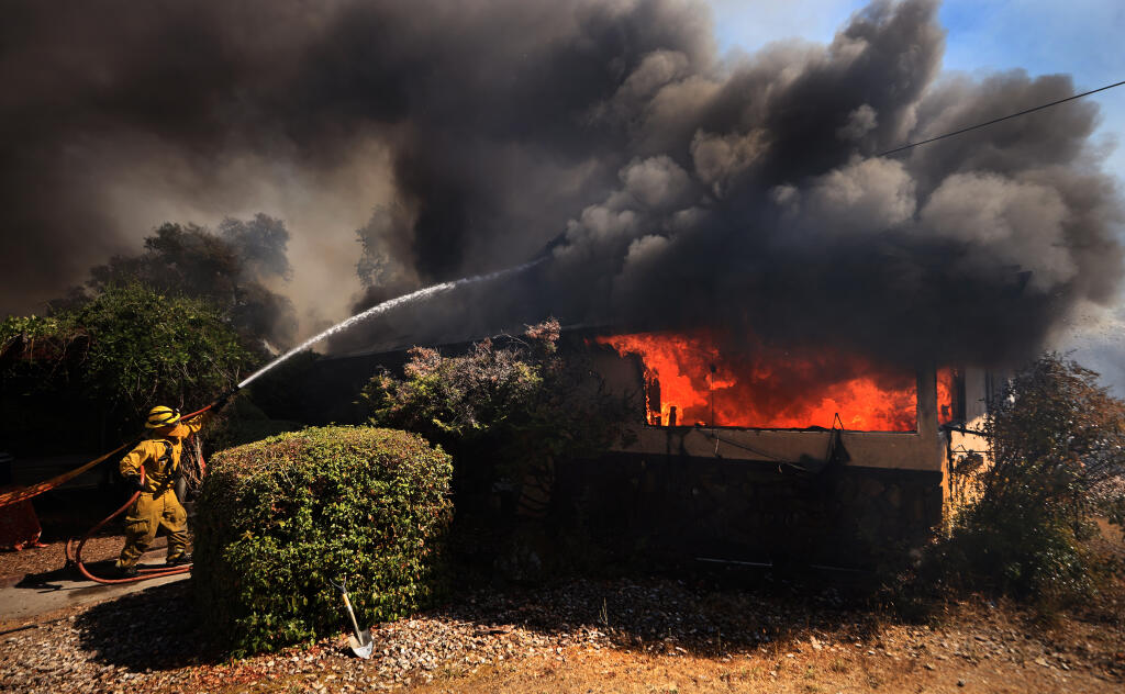Firefighters take a defensive stand against a home burning at Uva Dr. and W. School Way in Redwood Valley, ignited by an 80 acre wind whipped brush fire fed by tinder dry conditions, Wednesday, July 7, 2021.    (Kent Porter / The Press Democrat) 2021