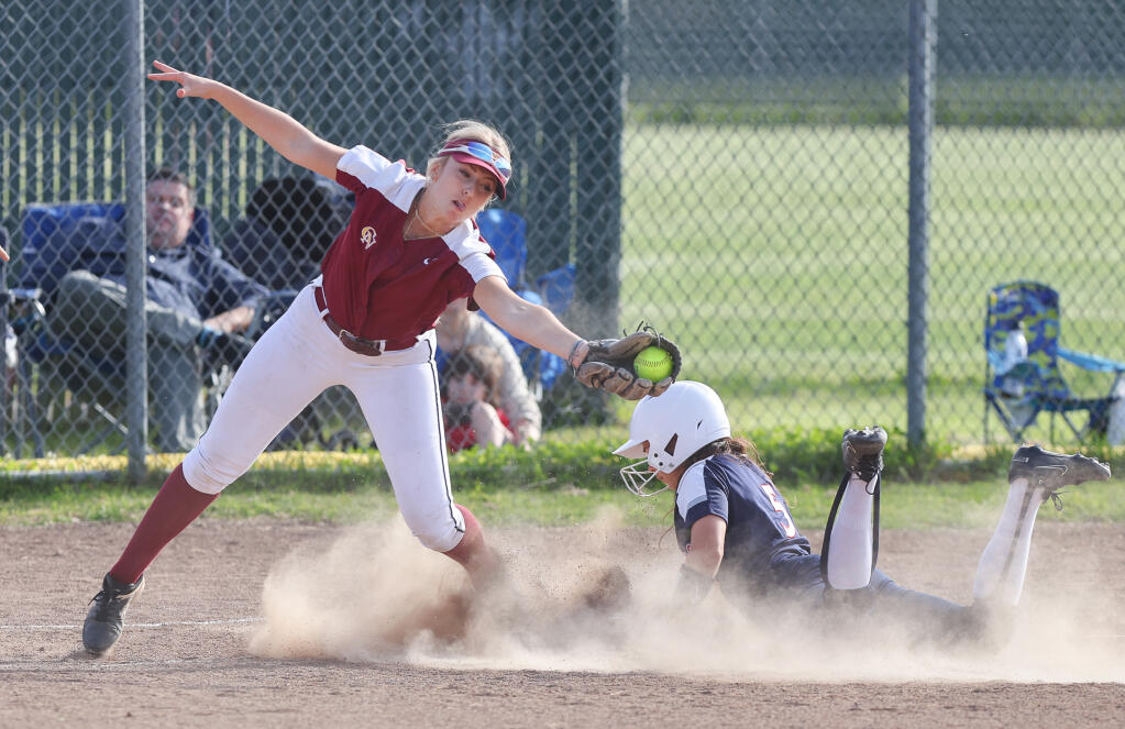 Cardinal Newman’s Andrea Mansbery stretches to catch the throw to third base, as Rancho Cotate’s Lillian Alves safely slides into the base, during their game in Rohnert Park on Thursday, April 18, 2024. (Christopher Chung/The Press Democrat)