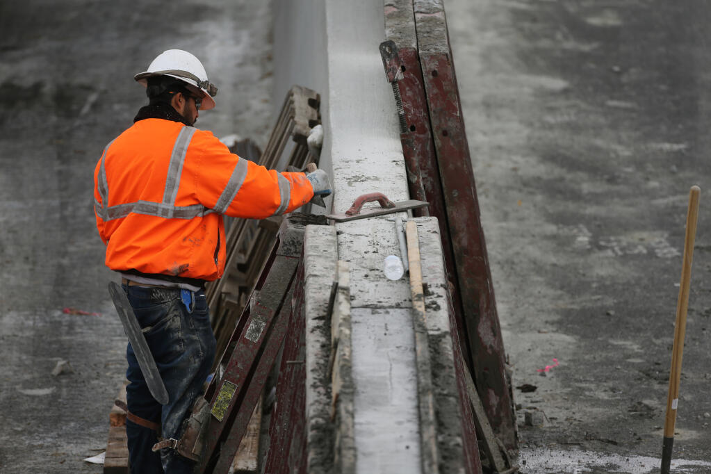 A construction worker smooths concrete as crews build a center barrier on Highway 101 in Petaluma, one of many who could see a pay increase. (BETH SCHLANKER/ The Press Democrat)