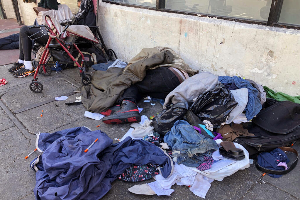 FILE - People sleep near discarded clothing and used needles on a street in the Tenderloin neighborhood in San Francisco, on July 25, 2019. The San Francisco Board of Supervisors will consider Thursday, Dec. 23, 2021, an emergency order to speed up the city's ability to stem the high number of overdose deaths in the notorious Tenderloin district. The emergency order is part of Mayor London Breed's plan to crack down on drug use and drug dealing in the neighborhood. (AP Photo/Janie Har, File)
