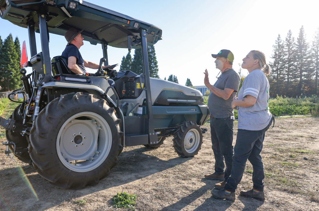 Bruce Mentzer, founder of Farm to Fight Hunger, left, sits in the cab of a new Monarch electric tractor, while talking to Zeke Guzman and Duskie Estes, executive director of Farm to Pantry, at JardÍn del Pueblo in Healdsburg, Wednesday, Nov. 8, 2023. (Christopher Chung / The Press Democrat file)