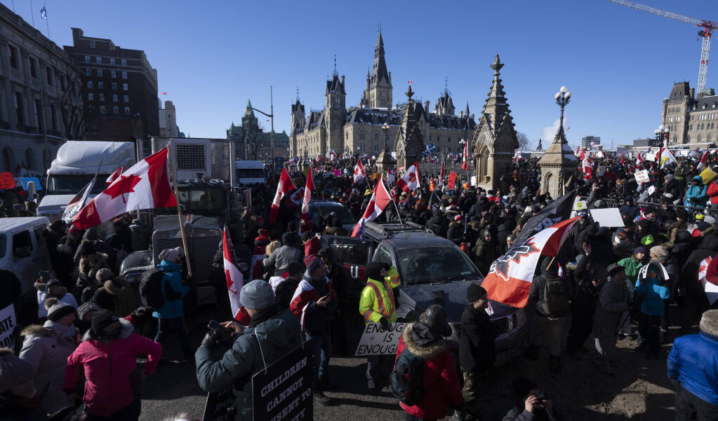 Protestors mingle around vehicles parked on Wellington St. in front of West Block and the Parliament buildings as they participate in a cross-country truck convoy protesting measures taken by authorities to curb the spread of COVID-19 and vaccine mandates in Ottawa on Saturday, Jan. 29, 2022. (Adrian Wyld/The Canadian Press via AP)