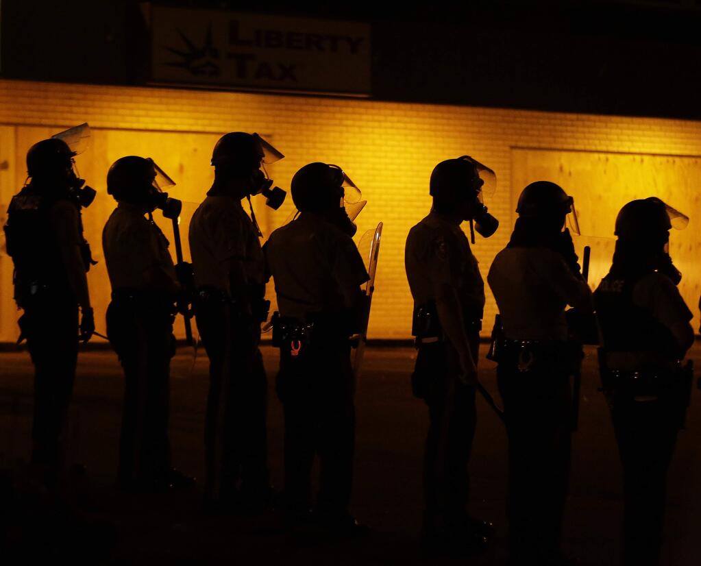 In this Aug. 17, 2014 file photo, police wait to advance after tear gas was used to disperse a crowd during a protest for Michael Brown, who was killed by a police officer in Ferguson, Mo. Since the shooting, many residents have been afraid to leave their homes at night as protesters clash with police in sometimes violent confrontations. (AP Photo/Charlie Riedel, File)