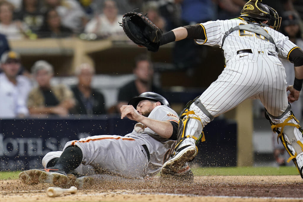 The San Francisco Giants’ Brandon Belt, below, scores off an RBI single by LaMonte Wade Jr. as San Diego Padres catcher Austin Nola looks on, above, during the ninth inning on Tuesday, Sept. 21, 2021, in San Diego. (Gregory Bull / ASSOCIATED PRESS)