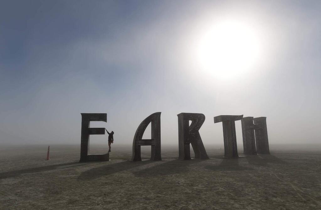 Anita Vranckx, of Belgium, hangs from the E of an Earth sculpture at Burning Man on a dusty morning on the playa in the Black Rock Desert near Gerlach, Nev., on Saturday Aug. 27, 2016. The annual festival is dedicated to community, art, self-expression and self-reliance. (Andy Barron/The Reno Gazette-Journal via AP)