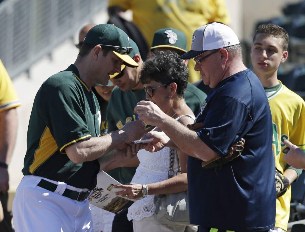 Michigan football coach Jim Harbaugh,left, signs autographs before a spring training baseball game between the Oakland Athletics and Los Angeles Angels, Saturday, March 7, 2015, in Mesa, Ariz. (AP Photo/Darron Cummings)