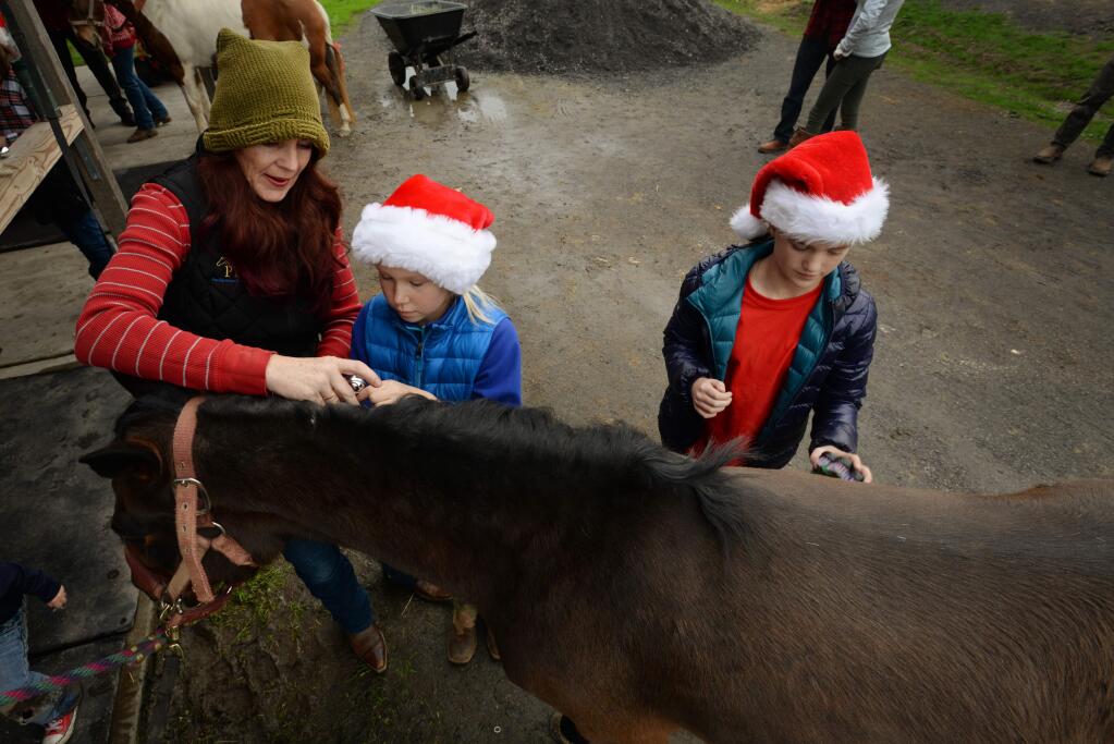 Sarah Hollingshead, left, and Else Popken, 11, tie on a jingle bell to Olive the horse while Nora Allen, 11, brushes her before leaving to Christmas carol on horse back Saturday evening at Circle ZN Ranch in Penngrove, California. December 22, 2018.(Photo: Erik Castro/for The Press Democrat)