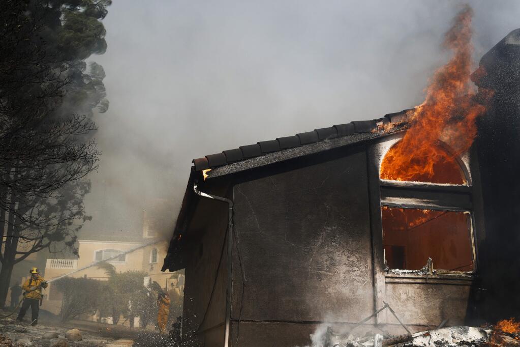 A firefighter works to put out a blaze burning a home Tuesday, Dec. 5, 2017, in Ventura, Calif. Authorities said the blaze broke out Monday and grew wildly in the hours that followed, consuming vegetation that hasn't burned in decades. (AP Photo/Jae C. Hong)