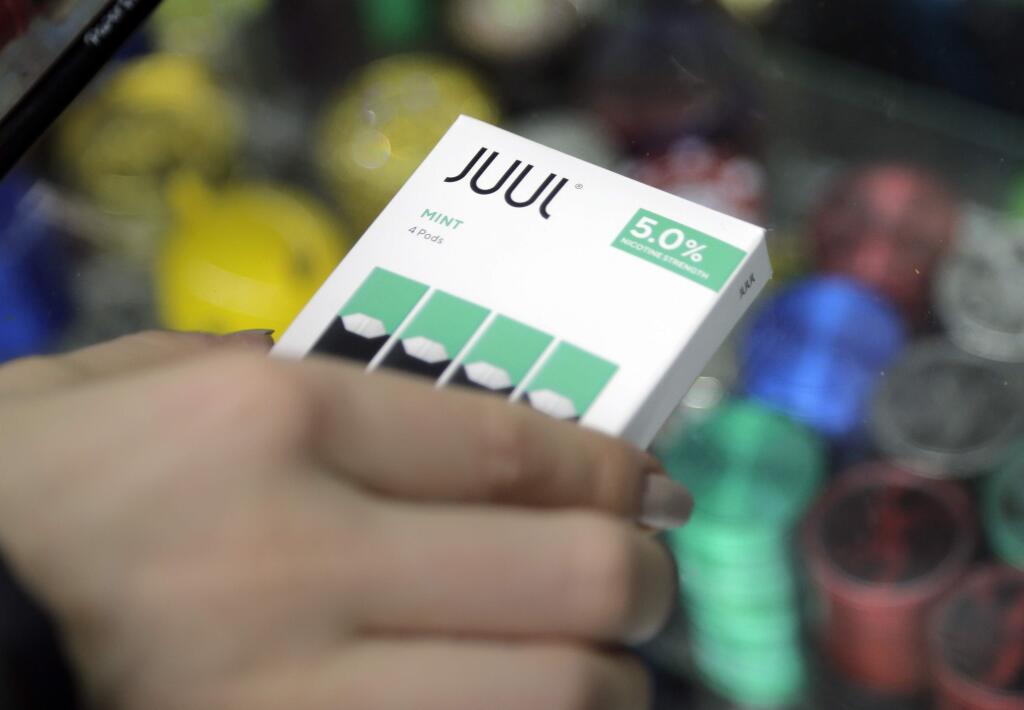 FILE - In this Dec. 20, 2018, file photo a woman buys refills for her Juul at a smoke shop in New York. The e-cigarette maker Juul Labs said Thursday, Nov. 7, 2019, that it will halt sales of its best-selling mint-flavored vaping pods. (AP Photo/Seth Wenig, File)