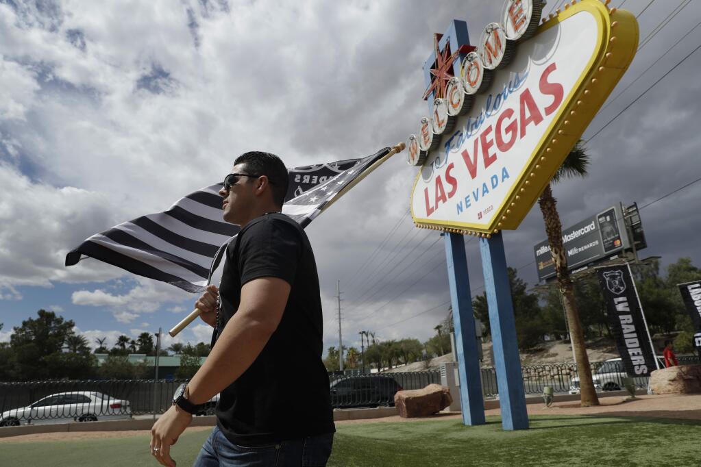 Matt Gutierrez carries a Raiders flag by a sign welcoming visitors to Las Vegas, Monday, March 27, 2017, in Las Vegas. (AP Photo/John Locher)