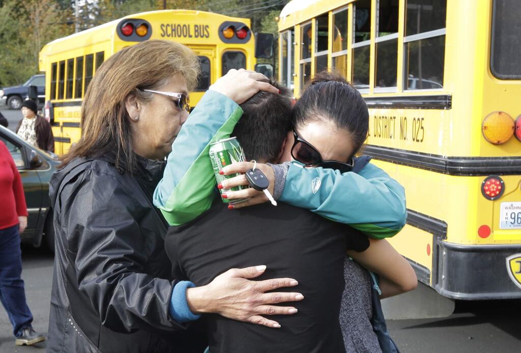 People embrace in front of school busses at a church Friday, Oct. 24, 2014, where students were taken to be reunited with parents following a shooting at Marysville Pilchuck High School in Marysville, Wash. (AP Photo/Ted S. Warren)